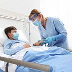 Masked child in hospital bed with masked medical professional at bedside.