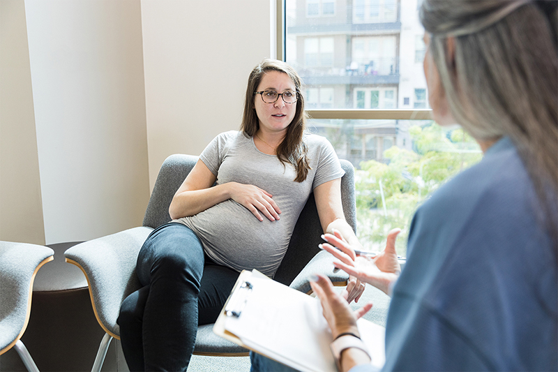 Pregnant person talking to medical professional holding a notebook.