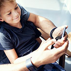 A man and a smiling little boy sitting in his lap look at a mobile phone.