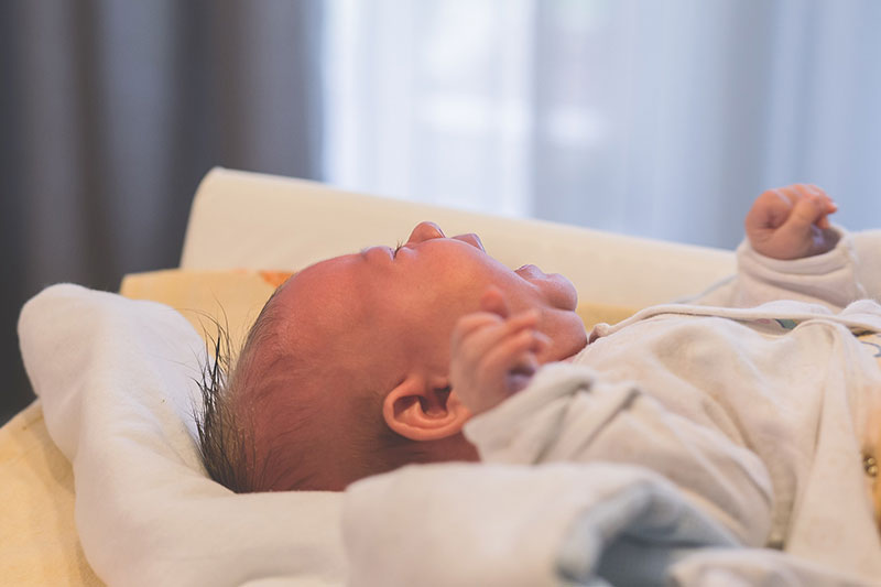 A crying baby lying on blankets.