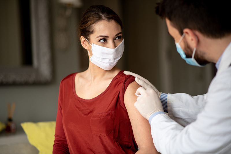 Health care worker swabbing a woman's arm. Both are wearing masks. 