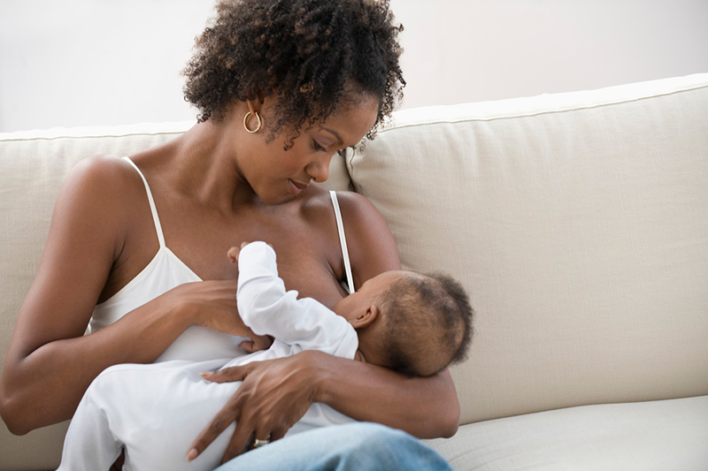 Mother sitting on a couch breast feeding a baby she holds in her lap.