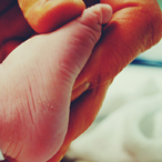 An adult holds the foot of a newborn, which has a hospital tag around its ankle.