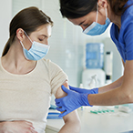 Pregnant person receiving an injection in the arm from a health care provider. Both are masked.