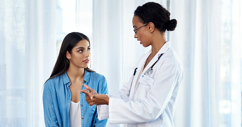 Patient, sitting on examination table, listening, while health care provider talks.