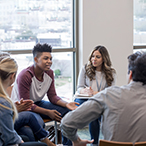 A diverse group of young adults sitting in a circle talking.