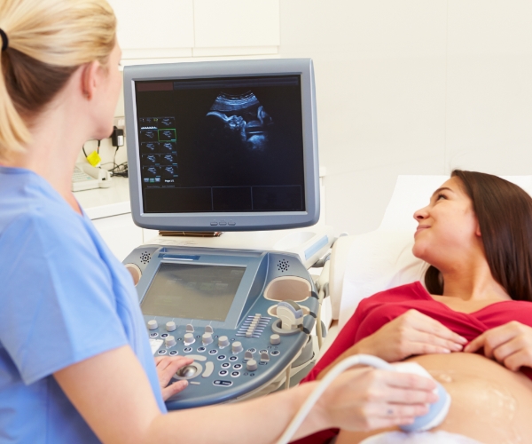 A health care provider giving a pregnant woman an ultrasound in a medical office.