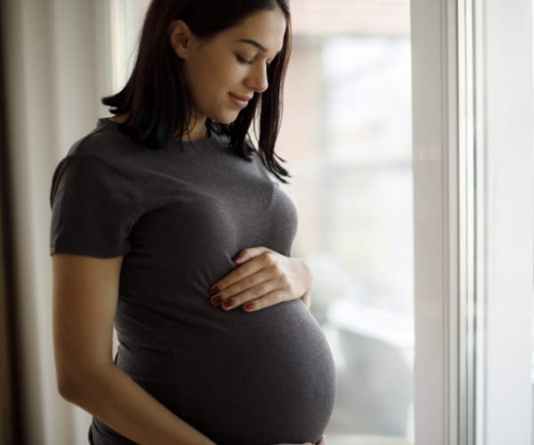 A pregnant woman looking at her belly in front of a window.