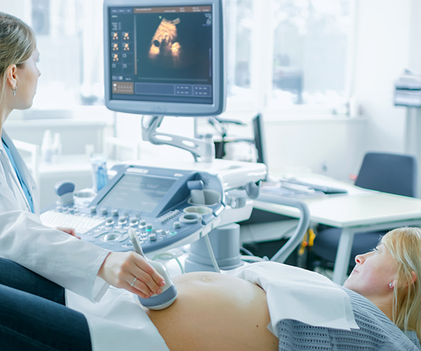 A healthcare provider uses an ultrasound machine on a pregnant parent’s belly as they both watch the screen in the hospital room.