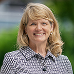 A smiling woman with trees and flowers in the background.