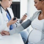 Health care provider taking blood pressure reading of pregnant person.