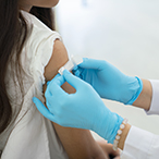 Gloved hands applying a small bandage to someone’s upper arm.