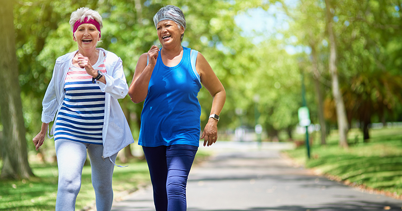 Two people smiling while walking briskly on a path.