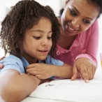 Child looks at open book while parent points at words on page.