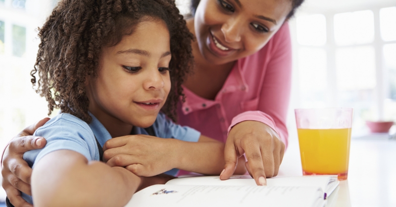 Child looks at open book while parent points at words on page.