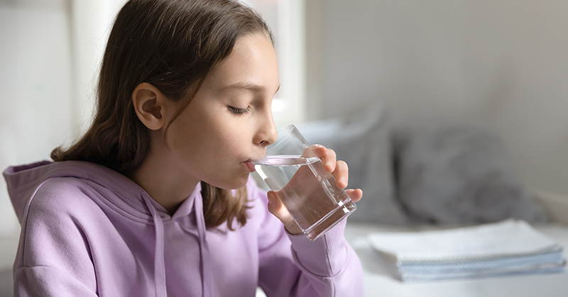 Teen girl drinking clear liquid from a clear glass.