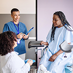 A woman sitting on an examination table interacts with two health care providers.