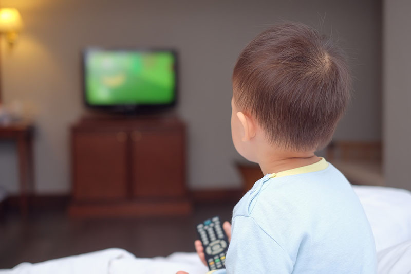 A young child with a remote control in his hand looking at a television screen.