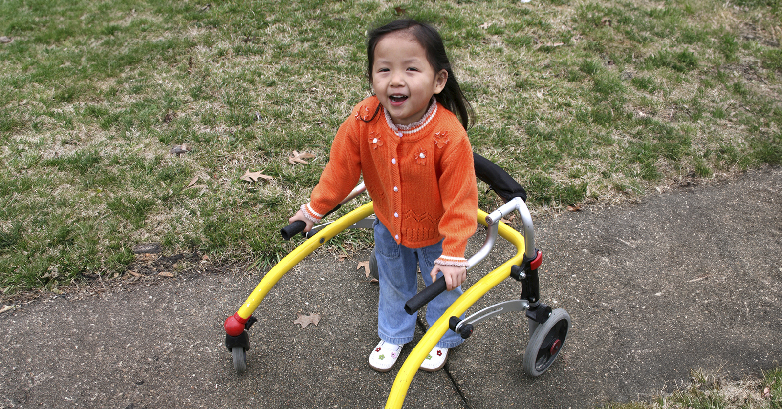 Toddler standing, holding the rails of an assisted walking device.