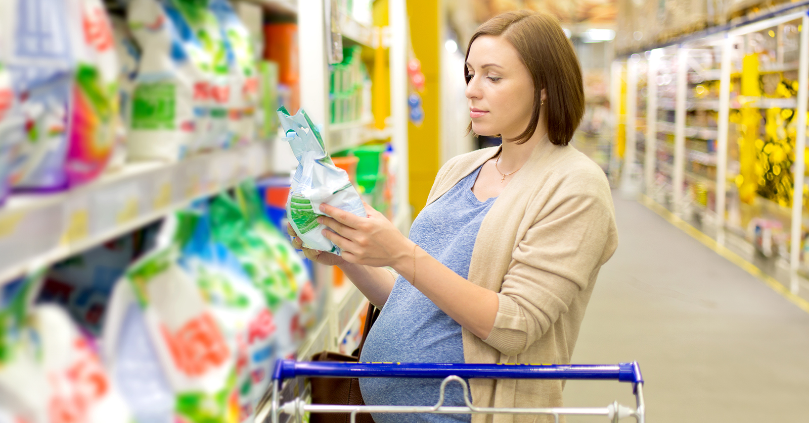 Pregnant woman behind a shopping cart reading a package label.