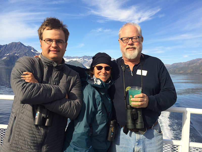 The family is smiling from a boat against a scenic background with a blue sky and mountains.