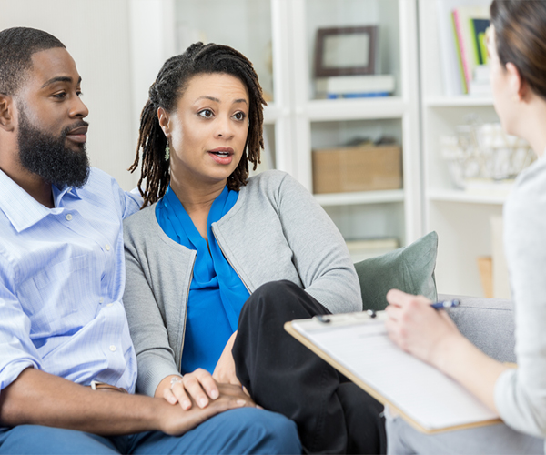Image of an African American couple speaking to a healthcare provider, who is holding a clipboard. 
