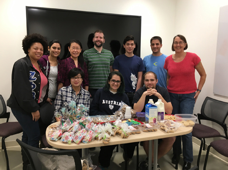 Lab members gather around a table with bags and containers of cookies.