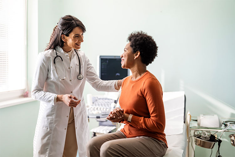 A woman in a doctor’s office is sitting down while speaking to a health care provider.