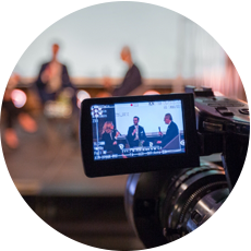 Close-up of camera flip screen showing a panel discussion being recorded. 