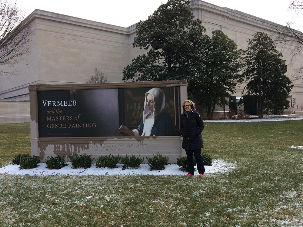 Dr. Bianchi smiles next to an outdoor sign advertising the exhibit.