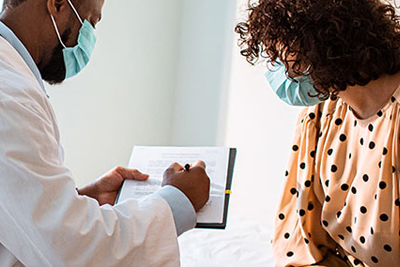 Woman consulting with her healthcare provider, who is showing her something he has written down in his exam notes. 