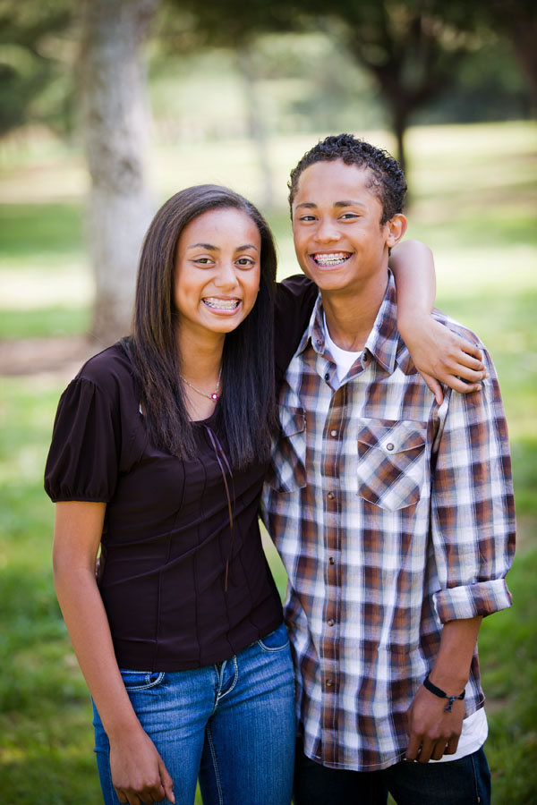 A smiling teenage girl and boy, both with braces. The girl’s arm is around the boy’s shoulders. 